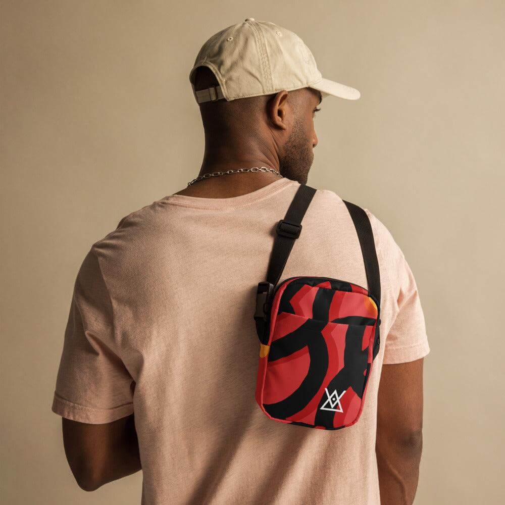 Man wearing Hora Magica Utility Crossbody Bag with red and black abstract design, adjustable strap and cap